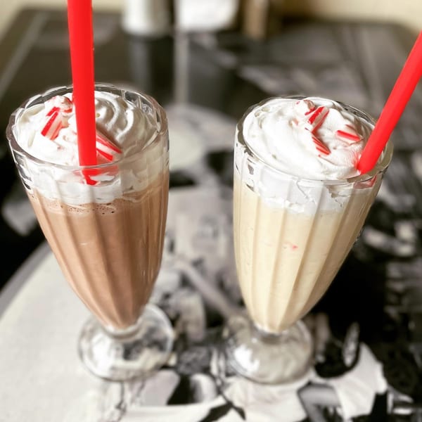 Two Mattie's Diner milkshakes, one chocolate and one vanilla, topped with whipped cream and candy canes.