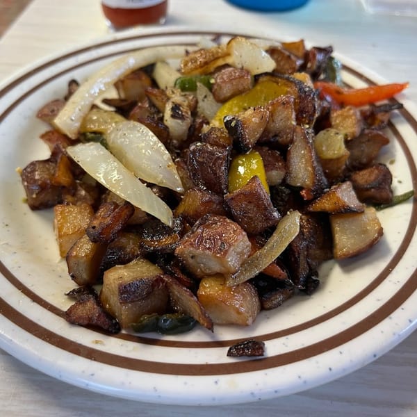 A close-up of Mattie's Diner home fries with onions and peppers on a white plate.