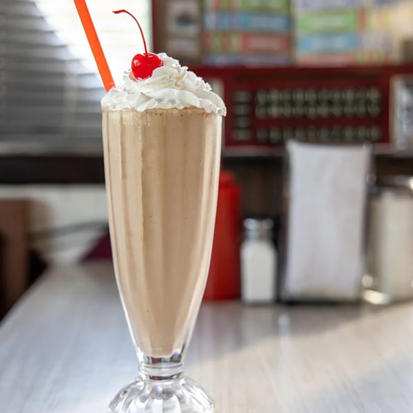 A Mattie's Diner milkshake with whipped cream, a cherry, and an orange straw.