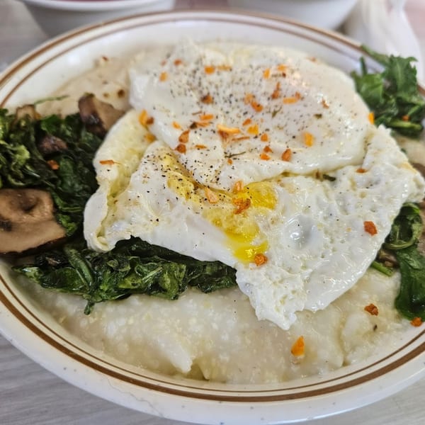 Creamy grits topped with two fried eggs, sautéed spinach, mushrooms, and spices in a diner setting.