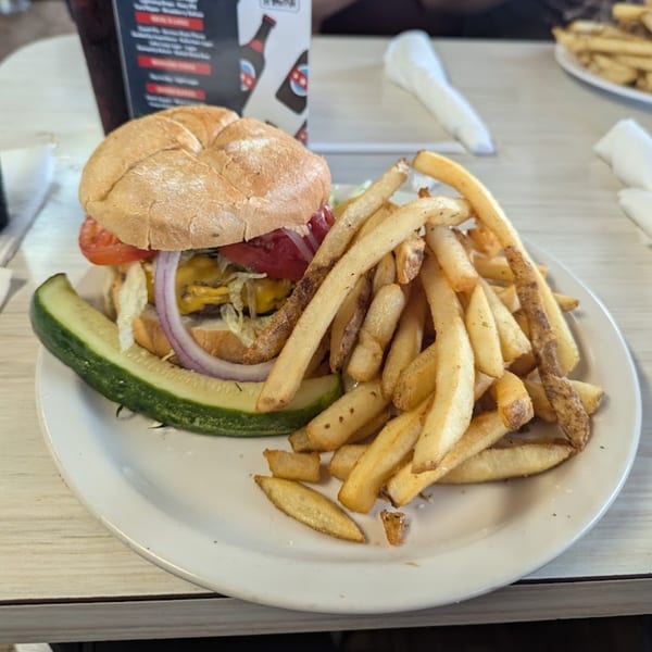 A Mattie's Diner cheeseburger with lettuce, tomato, onion, and a side of fries and pickle.