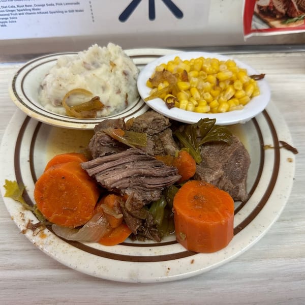 A diner plate with pot roast, carrots, onions, mashed potatoes, and corn.