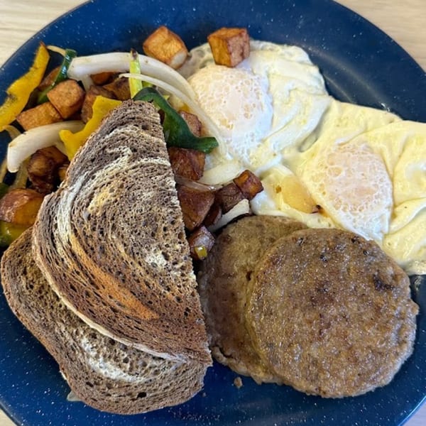 A diner breakfast plate with eggs, sausage patties, home fries, sautéed vegetables, and rye toast.