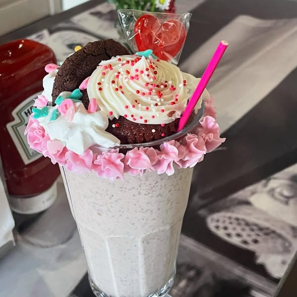 A Mattie's Diner milkshake topped with whipped cream, a cupcake, cookie, and heart lollipop.