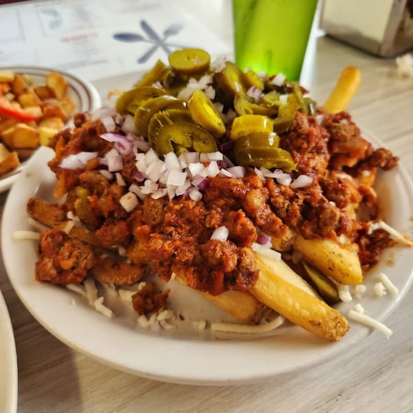 Mattie's Diner chili cheese fries topped with diced onions and sliced jalapeños, with a side of home fries.